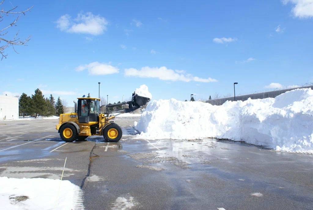 Heavy yellow front-end loader stacking snow into a large pile during commercial parking lot snow removal in Green Bay
