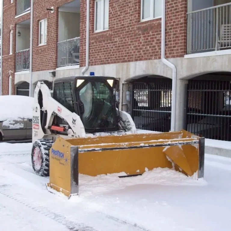 Bobcat skid steer loader with a box plow clearing snow outside a commercial residential building in Green Bay