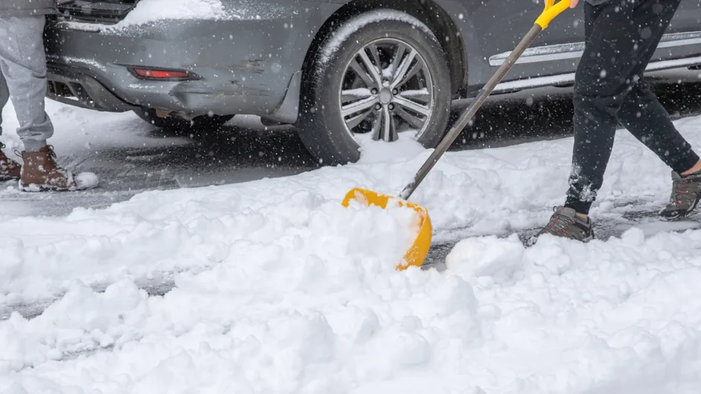 Person using a yellow snow shovel to clear snow around a parked car during Green Bay snow removal