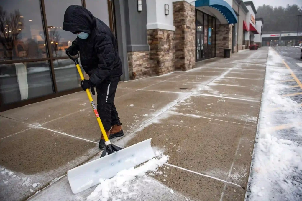 professional snow removal crew clearing store entrance walkways in Brown County to prevent slip-and-fall hazards and ensure city compliance.