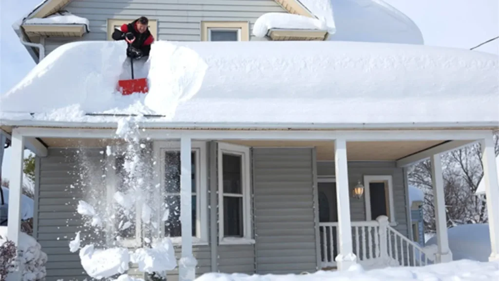 Snow being shoveled off a residential home roof in Brown County to avoid water leaks and freeze-thaw ice dam damage.