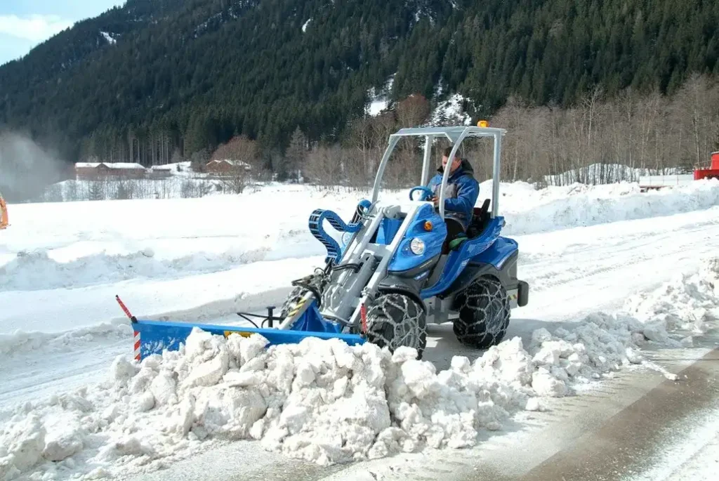 Compact blue tractor clearing heavy snow from a paved road in Green Bay