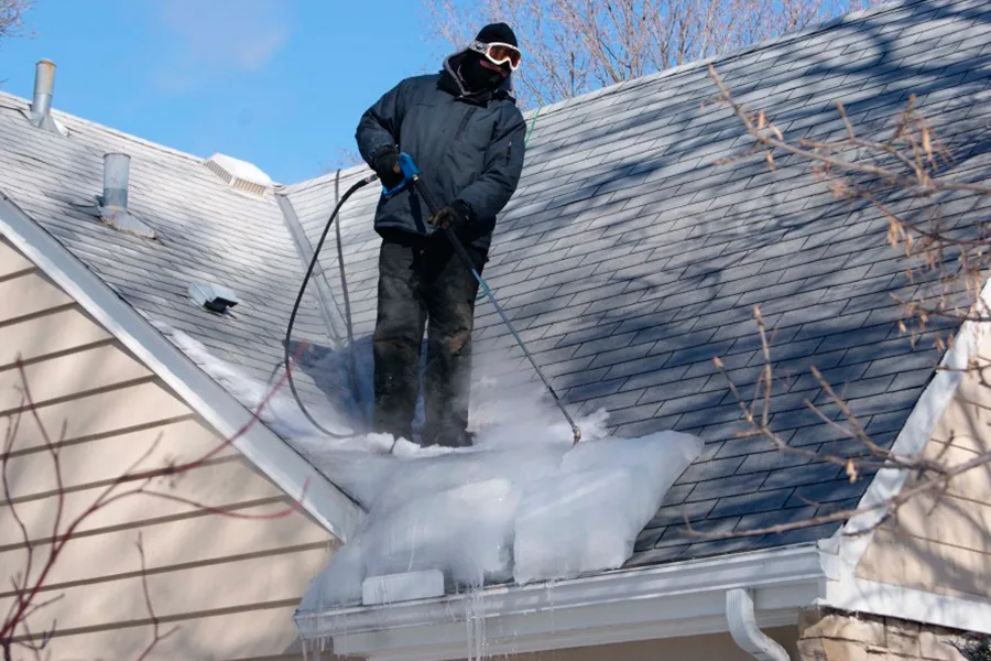 Professional technician using steam to remove an ice dam and thick ice accumulation from a residential roof in Green Bay