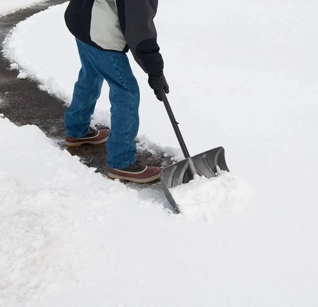 Worker shoveling snow from a concrete walkway during residential sidewalk clearing in Green Bay