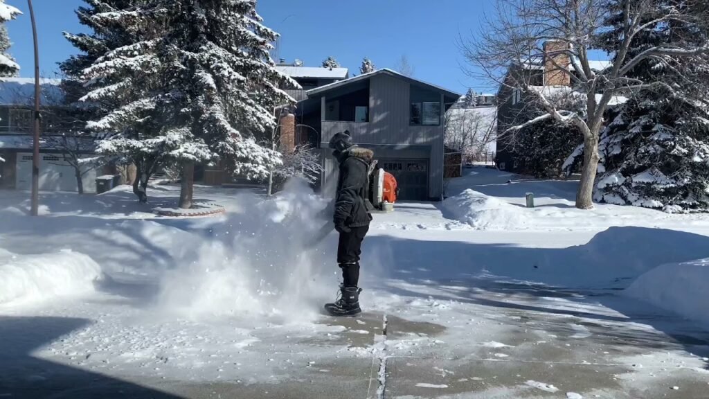 Operator using a powerful backpack blower to clear fresh snow from a residential driveway and sidewalk in Green Bay.