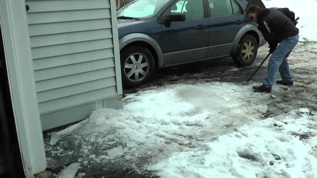 Man using an ice scraper tool to break up thick ice on a residential driveway for ice removal in Green Bay