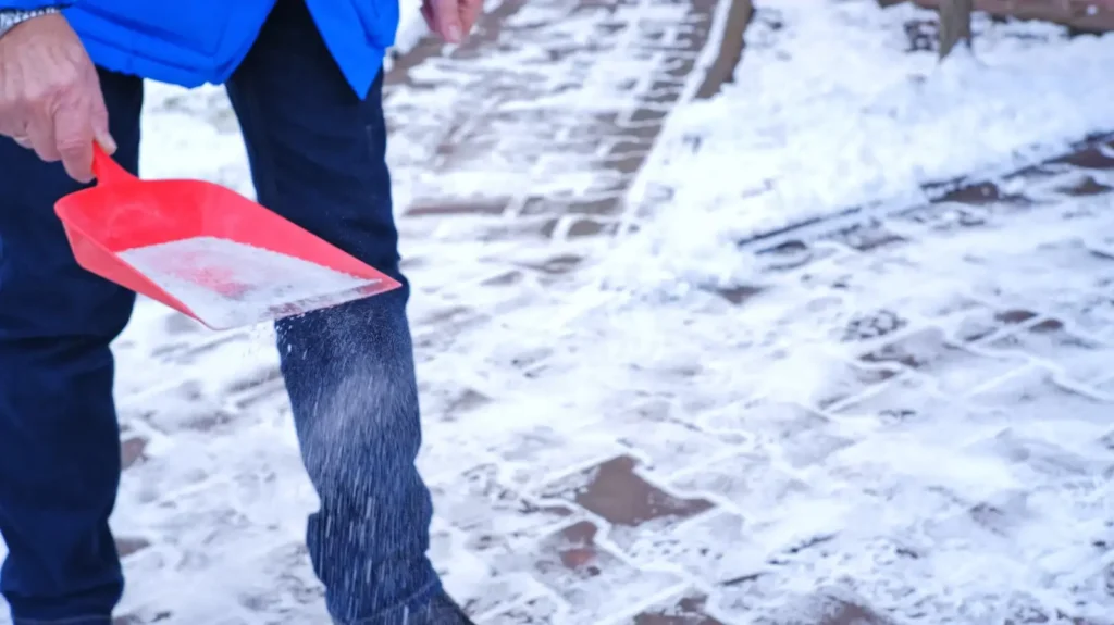Person spreading rock salt ice melt product on icy walkway for professional ice removal service in Green Bay